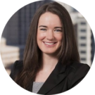 Young woman in a business suit smiling with buildings in the background, reflecting her expertise in commercial loans.