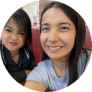 Two people sitting together, one adult and one child. The adult is smiling at the camera, while the child is making a playful face.