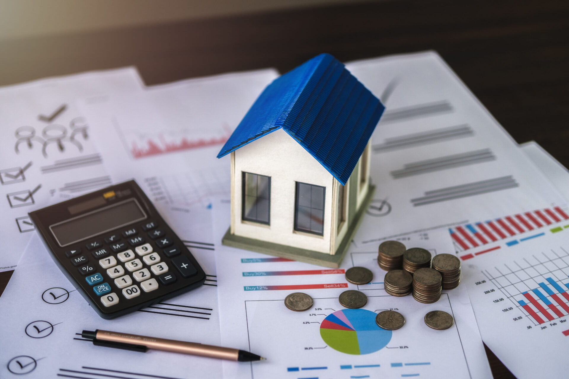 A miniature house, calculator, pen, and stacks of coins are placed on financial charts and documents, highlighting the critical role of Mortgage Brokers in navigating construction loans and investment loans for budding homeowners.