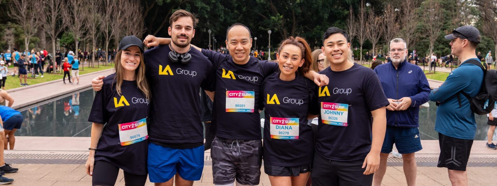 A group of five people wearing matching "LA Group" shirts with race bibs, posing together at the City 2 Surf.