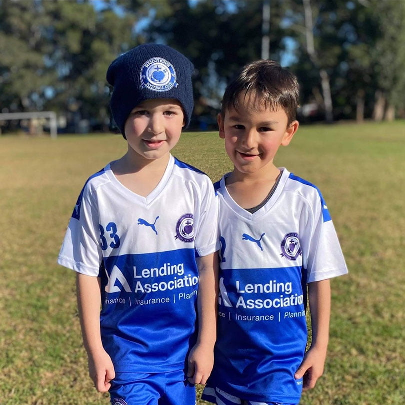 Two boys wearing blue and white soccer uniforms stand on a grass field.