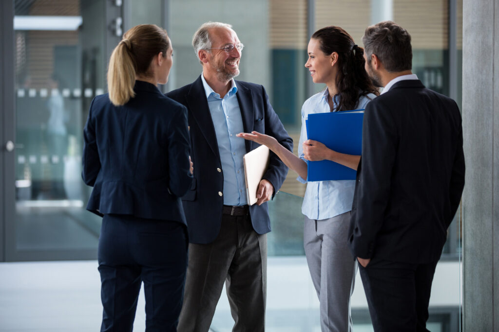 Four business professionals stand in a modern office, engaged in conversation.