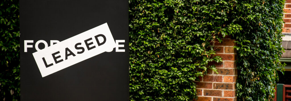 A "For Lease" sign with a "Leased" sticker is shown next to a brick wall covered in green ivy.