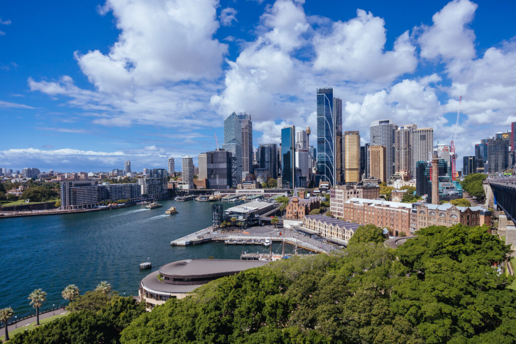 Aerial view of a vibrant cityscape featuring modern skyscrapers, a docked ferry, and surrounding greenery under a partially cloudy sky, showcasing an area bustling with businesses that benefit from commercial loans.