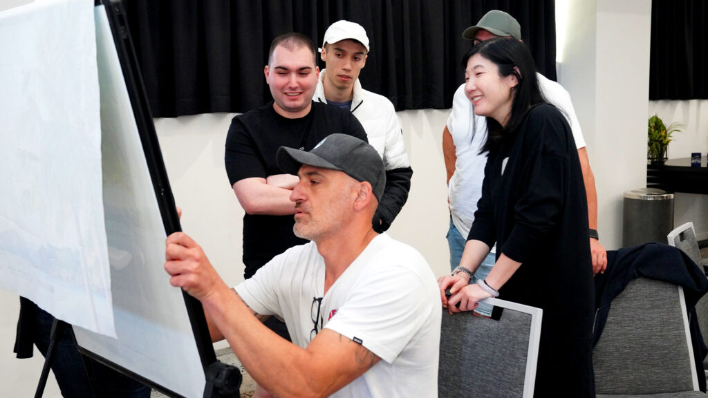 A group of people, with one person writing or drawing on a whiteboard, while four others observe and discuss investment loans.