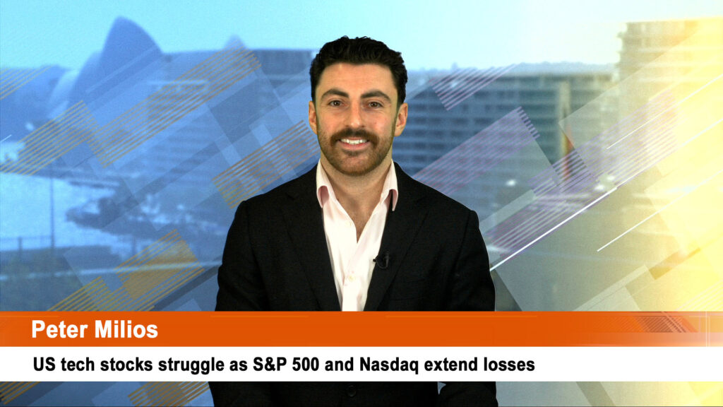 A man in a suit stands smiling in front of a background with mountains and buildings. Text: "Peter Milios. US tech stocks struggle as S&P 500 and Nasdaq extend losses."