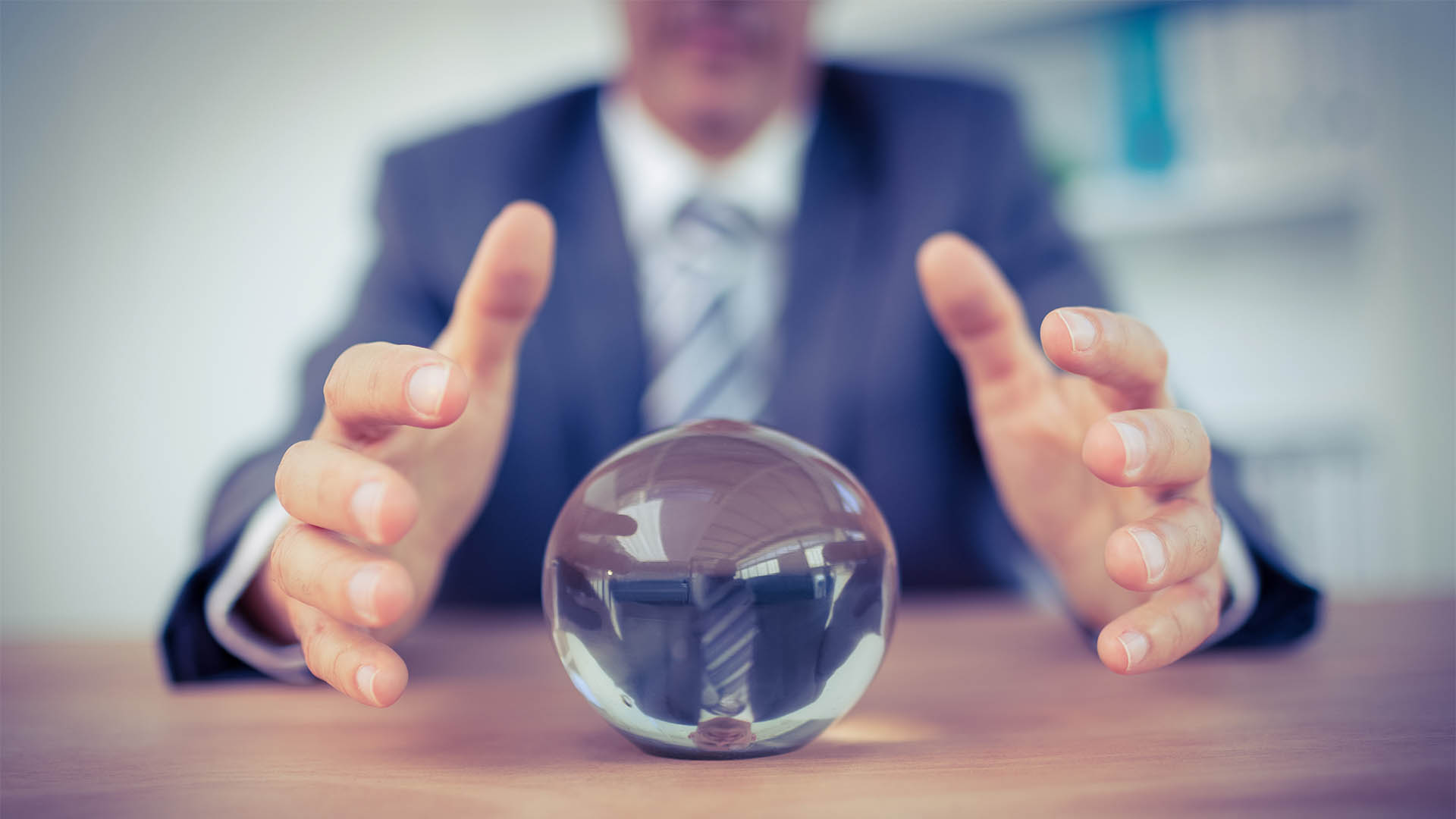 A person in a suit is sitting at a desk with hands hovering over a clear crystal ball, contemplating the future of business loans.