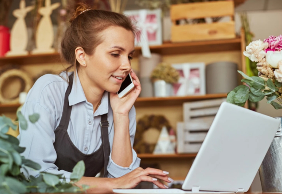Self-employed woman working on a laptop and phone, representing access to self-employed construction loans.