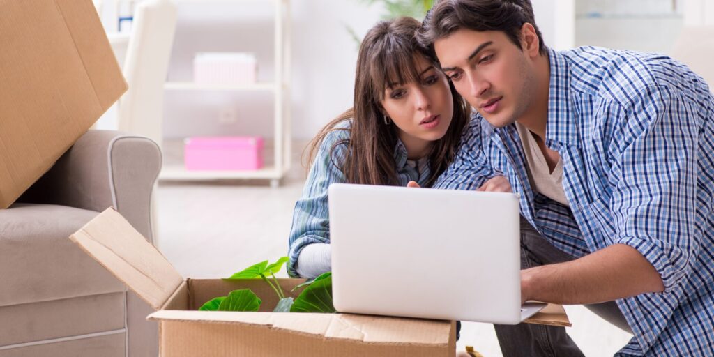A couple sitting among moving boxes, focused on a laptop as they plan smart strategies to pay off their mortgage faster.